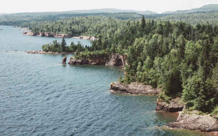 from a high vantage point, a the shore of a blue lake collides with a rocky shore lined with green trees